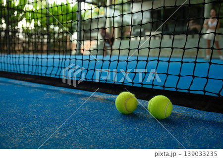 Padel players compete on a court with tennis balls nearby Padel players compete on a court with tennis balls nearby 139033235