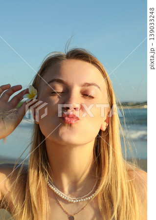 Woman smiles and poses with a flower near the beach Woman smiles and poses with a flower near the beach 139033248