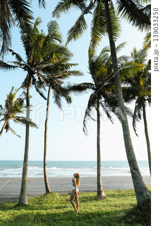 Woman walks along the beach surrounded by palm trees 139033250
