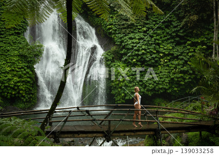 Person walks on a bridge near a waterfall and lush plants 139033258