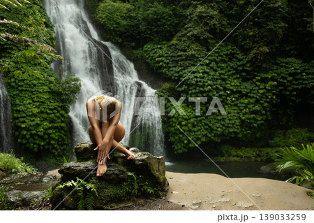 Woman sitting on a rock by a waterfall in Bali Woman sitting on a rock by a waterfall in Bali 139033259