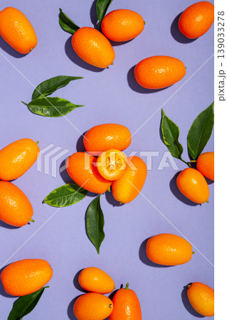 Kumquats are arranged with green leaves on a purple surface Kumquats are arranged with green leaves on a purple surface 139033278