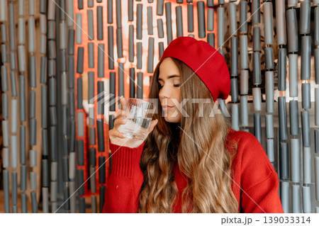 Woman Beret Water drinking from a glass in a cafe while wearing a red sweater for healthy hydration 139033314