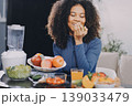 Young nutritionist showing bell peppers during an online video call consulting about healthy eating, sitting at home at a table with vegetables, laptop and measuring tape 139033479