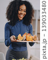 Young nutritionist showing bell peppers during an online video call consulting about healthy eating, sitting at home at a table with vegetables, laptop and measuring tape 139033480