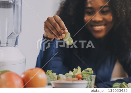 Young nutritionist showing bell peppers during an online video call consulting about healthy eating, sitting at home at a table with vegetables, laptop and measuring tape 139033483