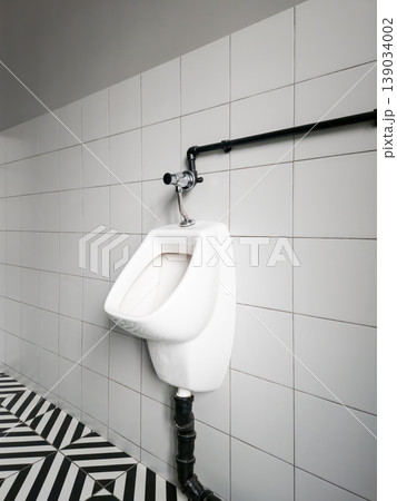Modern urinal installed in a restroom with black and white tile flooring Modern urinal installed in a restroom with black and white tile flooring 139034002