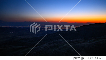 Nightfall over cityscape from elevated hillside with glowing lights Nightfall over cityscape from elevated hillside with glowing lights 139034325