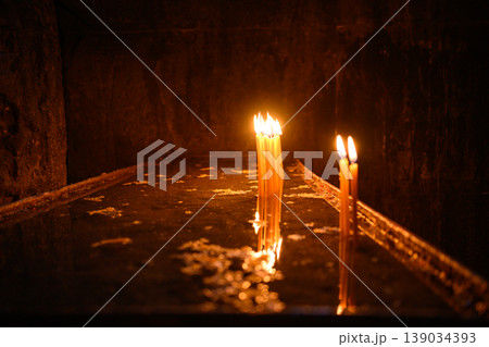 Lit candles in dark church interior, prayer and spirituality concept Lit candles in dark church interior, prayer and spirituality concept 139034393