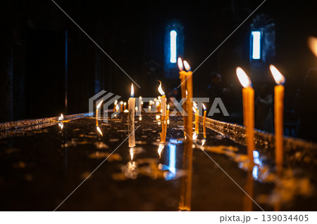 Rows of lit candles on wet floor inside church Rows of lit candles on wet floor inside church 139034405