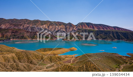 Turquoise lake surrounded by colorful mountain ridges under bright sky Turquoise lake surrounded by colorful mountain ridges under bright sky 139034434