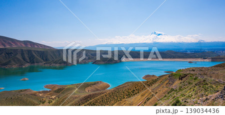 Landscape view of calm lake nestled between mountains and hills on sunny day Landscape view of calm lake nestled between mountains and hills on sunny day 139034436