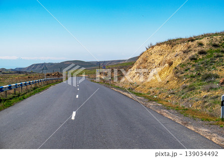 Long, empty road winds through arid hills under bright blue sky 139034492