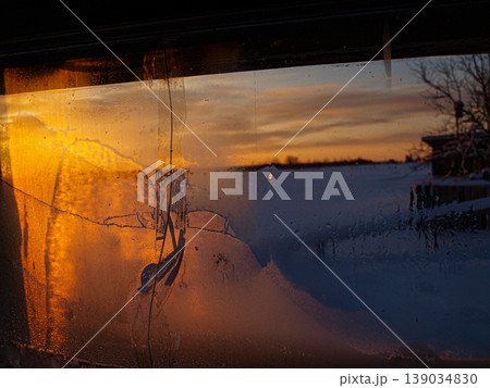 Red-orange sunset ray of the northern sun through a small window. Steam on cold glass creates a dramatic contrast between winter frost and warm light. Atmospheric ray in a moody interior. 139034830