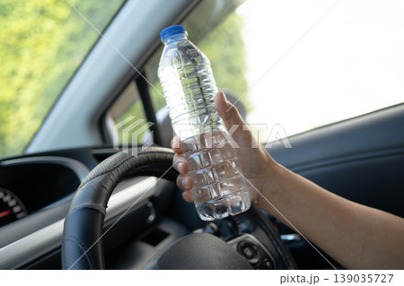 Asian woman driver hold cold water for drink in car, dangerous and risk an accident. 139035727