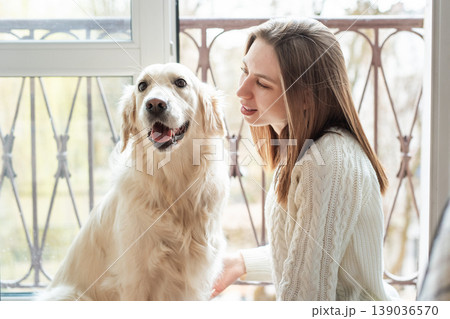 Woman bonding with golden retriever dog by window Woman bonding with golden retriever dog by window 139036570