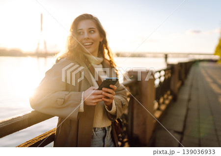 Young female city dweller with mobile phone standing on embankment alone. Woman shopping online. 139036933