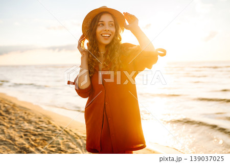 Carefree woman tourist walking along ocean sandy beach at sunset. Travel, weekend, lifestyle concept 139037025