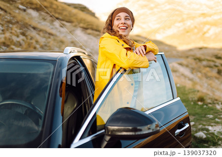 A cheerful traveler enjoying a scenic mountain view while sitting on the trunk. Travelling by car. A cheerful traveler enjoying a scenic mountain view while sitting on the trunk. Travelling by car. 139037320