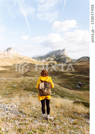 Traveler woman in yellow jacket enjoys hiking on sun. Hiking in mountains with backpacks. Adventure. 139037488