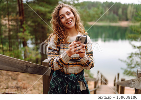 Portrait of a female traveler using her phone in the forest. Nice walk in the forest alone. Blogging Portrait of a female traveler using her phone in the forest. Nice walk in the forest alone. Blogging 139038186