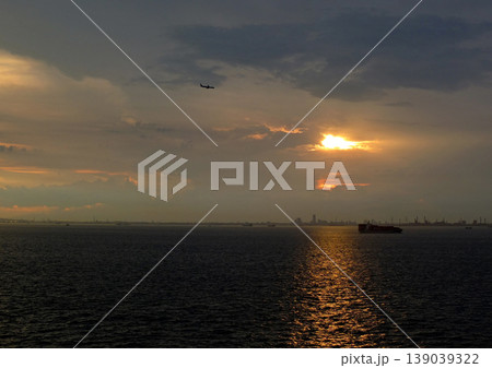 東京湾の夕暮れ時、海面が輝く。着陸する飛行機のシルエットとオレンジ色の夕日が印象的で綺麗だ。 東京湾の夕暮れ時、海面が輝く。着陸する飛行機のシルエットとオレンジ色の夕日が印象的で綺麗だ。 139039322