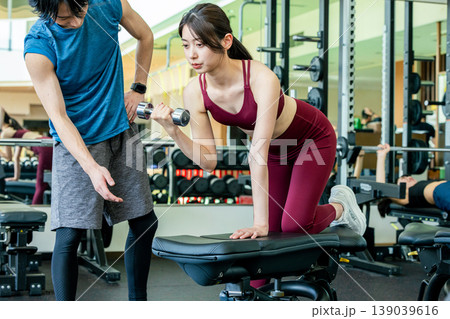 スポーツジムでウエイトトレーニングの説明を受ける若い女性 スポーツジムでウエイトトレーニングの説明を受ける若い女性 139039616