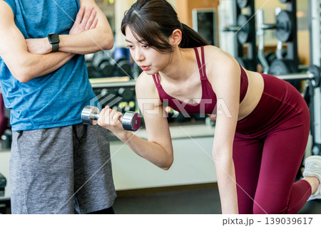 スポーツジムでウエイトトレーニングの説明を受ける若い女性 スポーツジムでウエイトトレーニングの説明を受ける若い女性 139039617