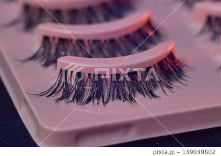 Macro eyelash trays under purple light, lash artist prep station showcasing strip lashes on glossy white trays, neon lighting casting pink highlights, shallow depth 139039802