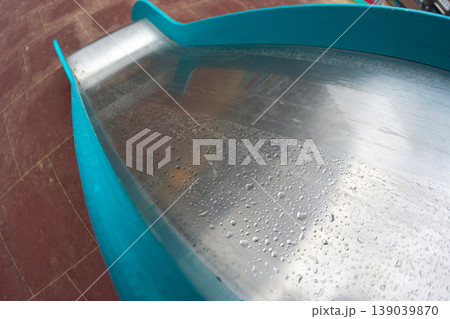 Water collects on a shiny metal slide at a playground. The slide is surrounded by a colorful play area Water collects on a shiny metal slide at a playground. The slide is surrounded by a colorful play area 139039870