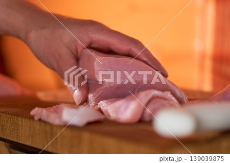 Closeup of hands cutting chicken on wood. Detailed view of hands expertly cutting raw chicken on wooden surface in warm kitchen lighting Closeup of hands cutting chicken on wood. Detailed view of hands expertly cutting raw chicken on wooden surface in warm kitchen lighting 139039875