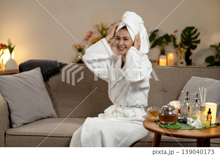 Asian woman relaxing self care spa treatment wearing white bathrobe towel her head cozy home living room setting wellness beauty routine at home Asian woman relaxing self care spa treatment wearing white bathrobe towel her head cozy home living room setting wellness beauty routine at home 139040173