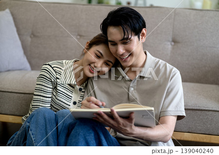 Asian adult couple reading book happily together in cozy home living room partners sharing quiet learning moment domestic lifestyle Asian adult couple reading book happily together in cozy home living room partners sharing quiet learning moment domestic lifestyle 139040240