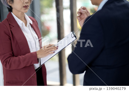 Asian business woman executive presenting document to male colleague during meeting professional office team collaboration workspace discussion corporate strategy project review 139040279