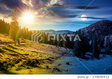 day meet night. fir trees on a meadow down the hill to coniferous forest in mountains of Romania nature. sun and moon over view of remote colorful forest at the foot of a mountain in autumn 139040412