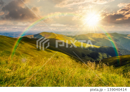 sunset over mountain landscape with alpine meadow in dappled light. carpathian mountain scenery in summer. view in to the distant valley landscape. rolling hills and grassy meadow under the rainbow sunset over mountain landscape with alpine meadow in dappled light. carpathian mountain scenery in summer. view in to the distant valley landscape. rolling hills and grassy meadow under the rainbow 139040414