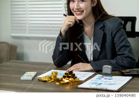Asian businesswoman managing wealth investments financial planning analyzing market data with gold money currency office environment 139040490
