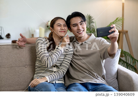Young Asian couple take selfie together on sofa at home enjoying happy intimate moment share joyful lifestyle modern smartphone technology 139040609