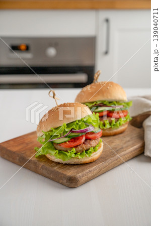 Two beef burgers with tomato, cheese, and lettuce on a cutting board on a light table Two beef burgers with tomato, cheese, and lettuce on a cutting board on a light table 139040711