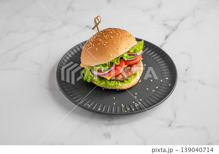 Beef burger with tomato, cheese, and lettuce on a black plate on a marble background. Beef burger with tomato, cheese, and lettuce on a black plate on a marble background. 139040714