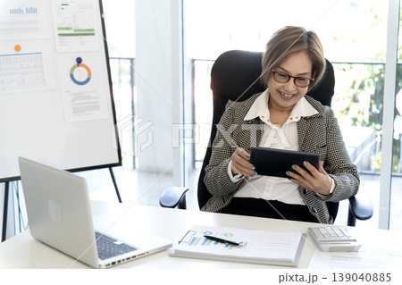 Asian adult businesswoman using digital tablet for work office setting analyzing business data marketing reports preparing financial strategy remote work solution 139040885
