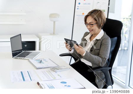 Asian professional woman conducting business analysis with digital tablet laptop modern office setting work productivity happy focused financial data review 139040886