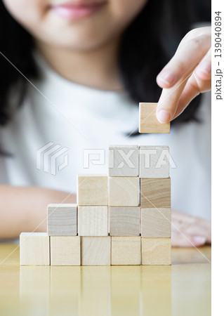 Wooden blocks and cubes form rising step shapes on a table in front of a child, combining gradual learning progress with playful problem solving and early thinking development. 139040894