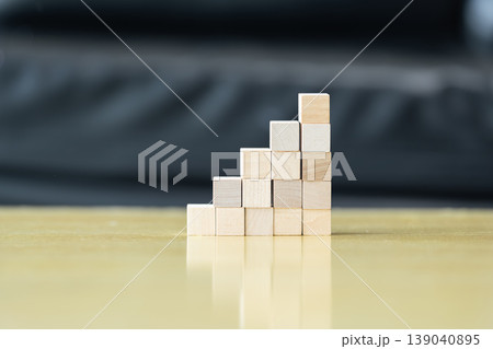 Wooden blocks and cubes form rising step shapes on a table in front of a child, combining gradual learning progress with playful problem solving and early thinking development. Wooden blocks and cubes form rising step shapes on a table in front of a child, combining gradual learning progress with playful problem solving and early thinking development. 139040895