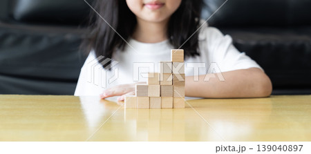 Wooden blocks and cubes form rising step shapes on a table in front of a child, combining gradual learning progress with playful problem solving and early thinking development. Wooden blocks and cubes form rising step shapes on a table in front of a child, combining gradual learning progress with playful problem solving and early thinking development. 139040897