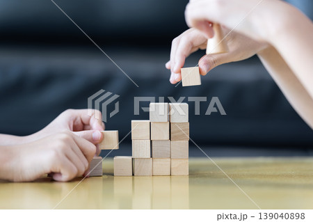Wooden blocks and cubes form rising step shapes on a table in front of a child, combining gradual learning progress with playful problem solving and early thinking development. 139040898