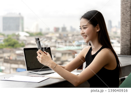Young Asian professional woman uses smartphone video call smiling remote working cityscape cafe balcony outdoor business meeting connection Young Asian professional woman uses smartphone video call smiling remote working cityscape cafe balcony outdoor business meeting connection 139040916
