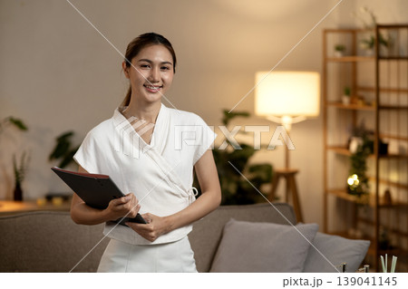 Asian adult woman smiling holding document folder offering professional wellness service in cozy indoor setting Asian adult woman smiling holding document folder offering professional wellness service in cozy indoor setting 139041145