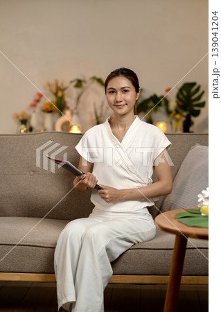 Asian adult woman spa therapist professional smiling holding clipboard for wellness client welcome relaxation beauty health care serene environment consultation booking Asian adult woman spa therapist professional smiling holding clipboard for wellness client welcome relaxation beauty health care serene environment consultation booking 139041204