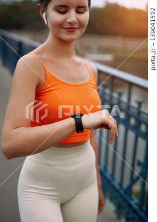 Fitness. Woman Checking Smart Watch Before Workout and Using Wireless Earbud. Girl listening to music using earphones. Fitness. Woman Checking Smart Watch Before Workout and Using Wireless Earbud. Girl listening to music using earphones. 139041592